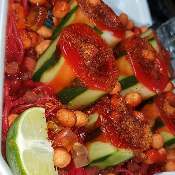 Spicy cucumber slices with chili powder, hot sauce, peanuts, and a lime wedge.