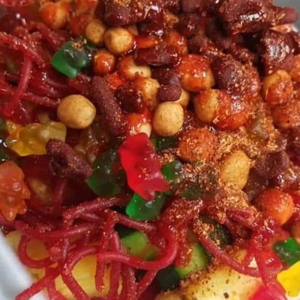 Close-up of a colorful Mexican candy mix with red gummy worms, peanuts, and fruit.