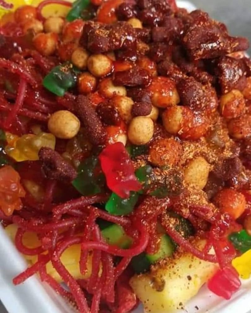 Close-up of a colorful Mexican candy mix with red gummy worms, peanuts, and fruit.