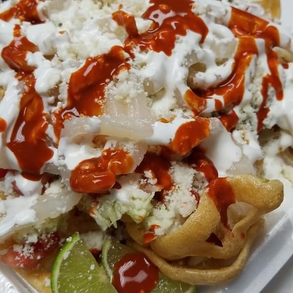 Close-up of a Mexican dish with white cheese, red sauce, and lime wedges.