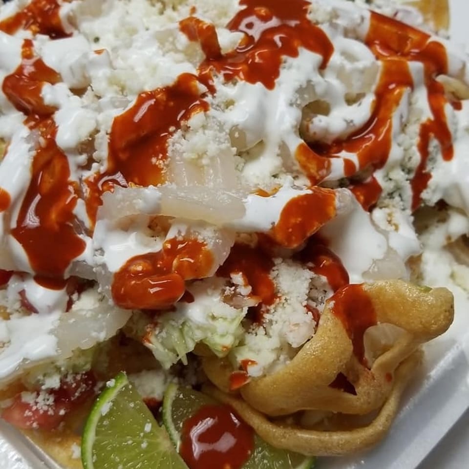 Close-up of a Mexican dish with white cheese, red sauce, and lime wedges.