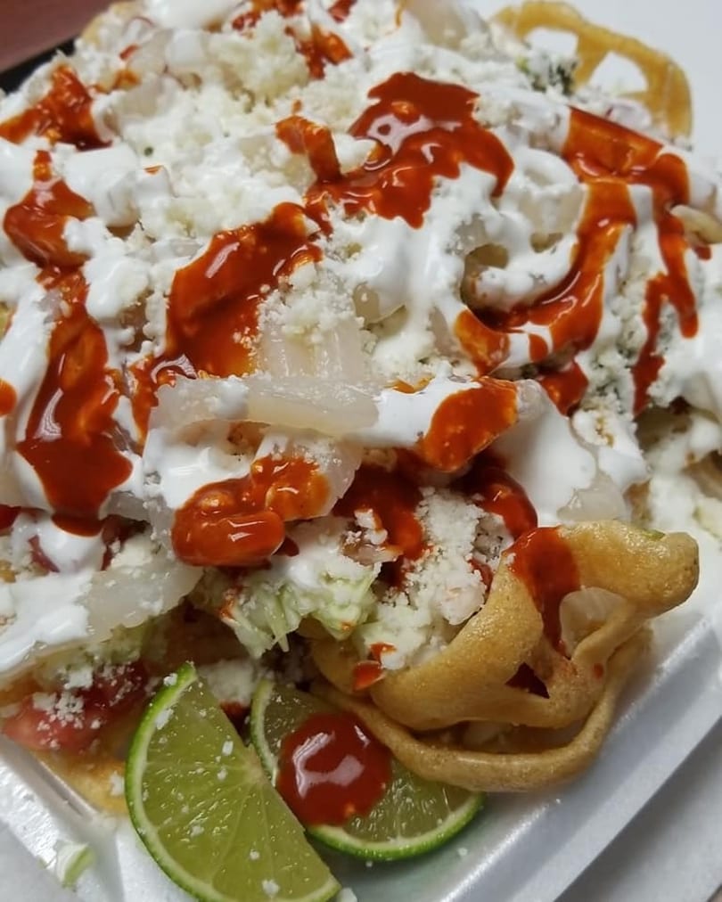 Close-up of a Mexican dish with white cheese, red sauce, and lime wedges.