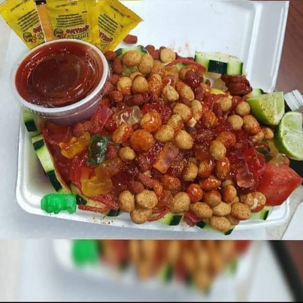 A vibrant Mexican snack with peanuts, gummy candies, cucumber, watermelon, lime, and chili sauce.