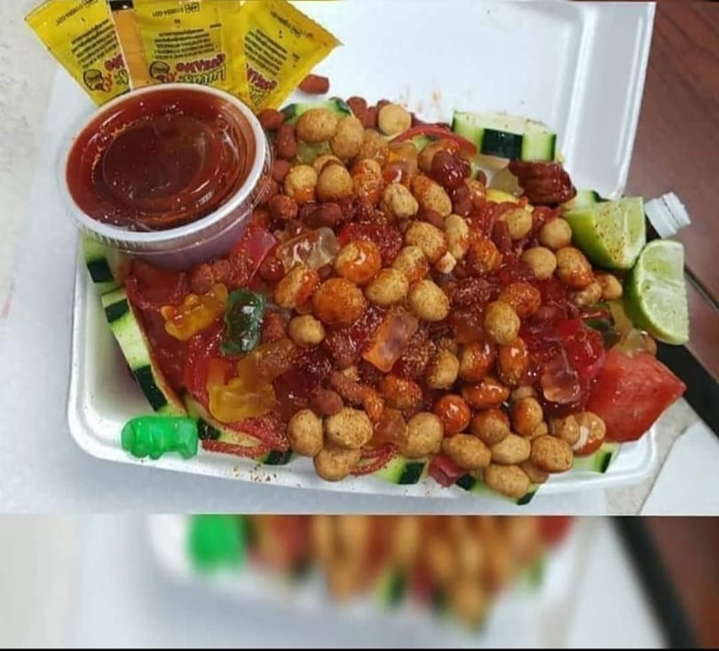 A vibrant Mexican snack with peanuts, gummy candies, cucumber, watermelon, lime, and chili sauce.