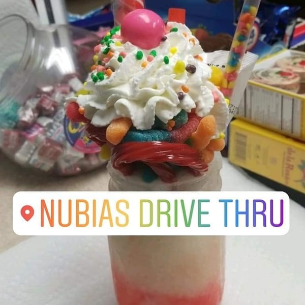 A colorful dessert drink topped with whipped cream, sprinkles, candies, and a pink gumball.