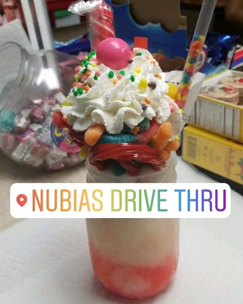 A colorful dessert drink topped with whipped cream, sprinkles, candies, and a pink gumball.