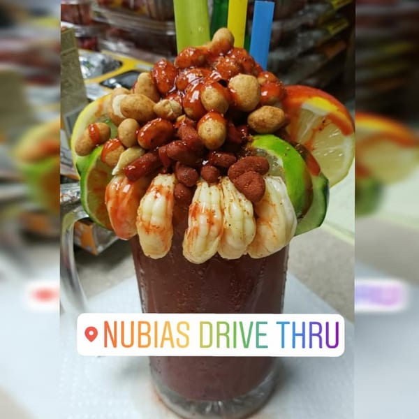 A michelada drink overflowing with shrimp, peanuts, and lime slices, with colorful straws.