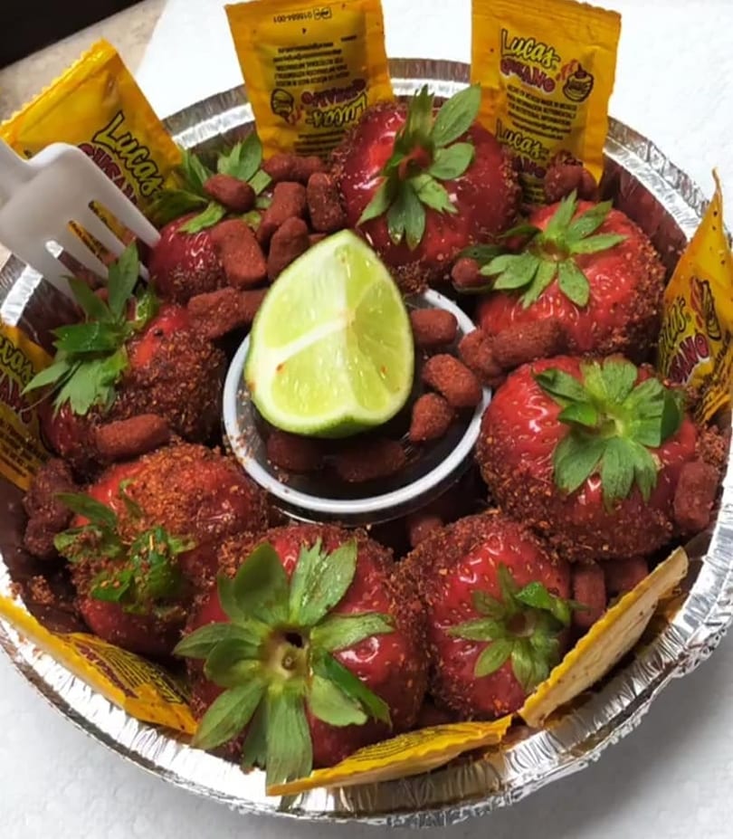 Strawberries coated in chili powder, with a lime wedge and Lucas candies in a foil tray.