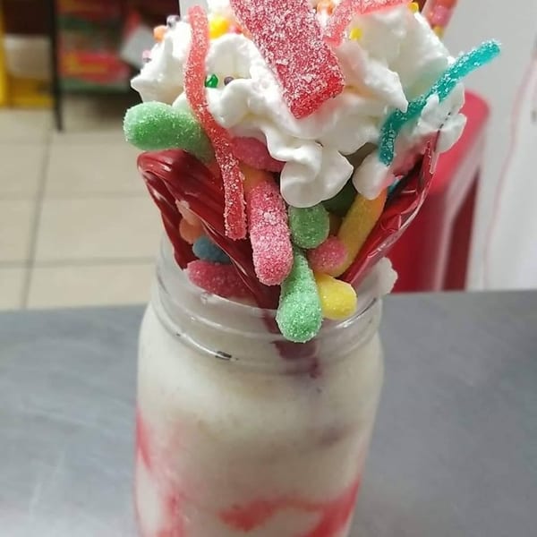A milkshake in a mason jar topped with whipped cream, colorful gummy candies, and sprinkles.