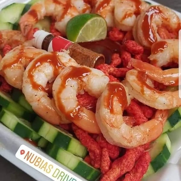 Shrimp cocktail with hot sauce, lime, cucumber slices, and red spicy snacks.