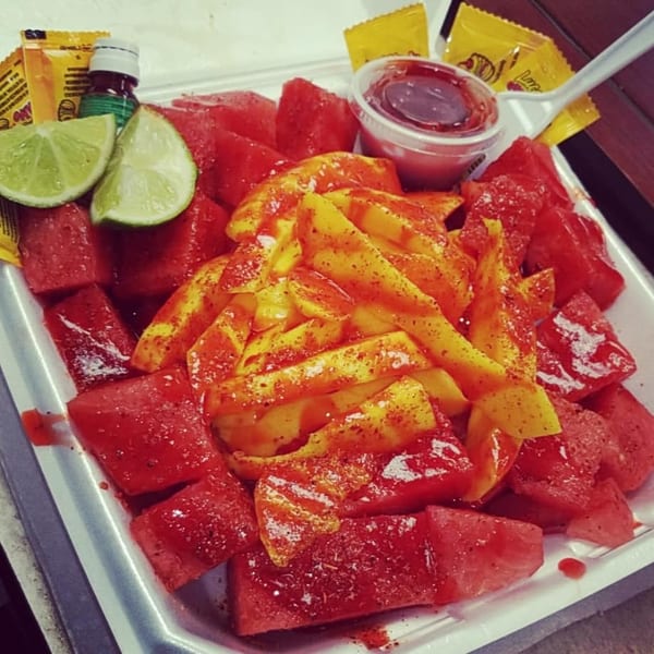 Watermelon and mango slices topped with chili powder and hot sauce, with lime wedges.