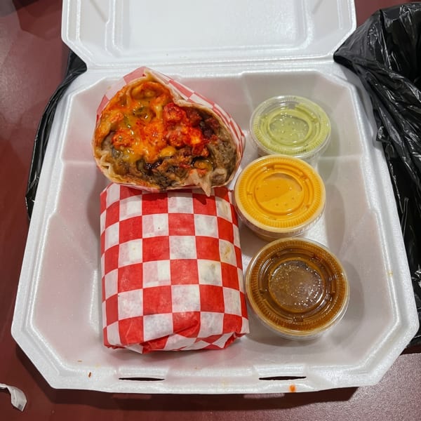 A takeout container with a burrito, one wrapped in red and white paper, and three sauce cups.