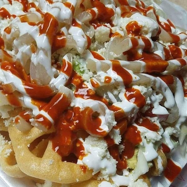 Close-up of a Mexican street snack with chicharrones, cabbage, cheese, crema, and hot sauce.