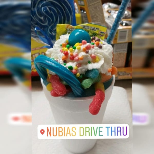 A white cup filled with whipped cream, colorful sprinkles, gummy worms, and blue candy.