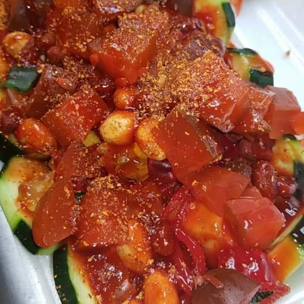Close-up of a vibrant Mexican fruit salad with red cubes, gummy bears, and chili powder.