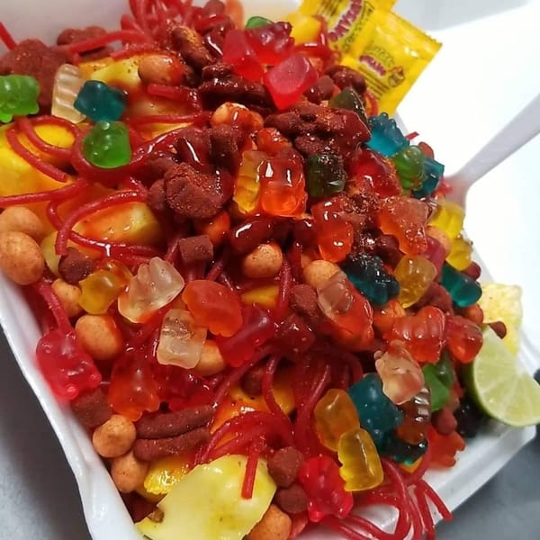 Colorful Mexican candy mix with gummy bears, peanuts, and chili sauce, served with a lime wedge.