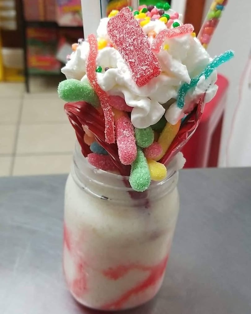 A milkshake in a mason jar topped with whipped cream, colorful gummy candies, and sprinkles.