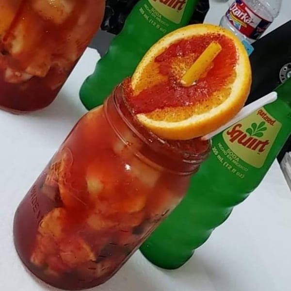 A red drink in a mason jar, garnished with an orange slice and chili powder.