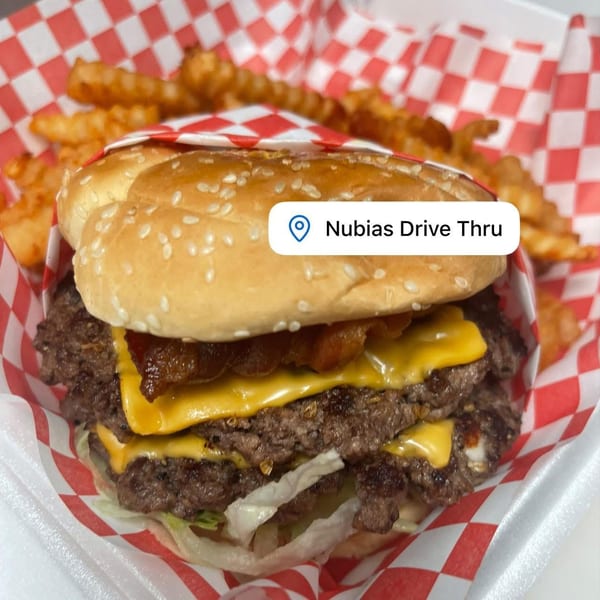Double cheeseburger with bacon, lettuce, and crinkle-cut fries in a red and white checkered basket.