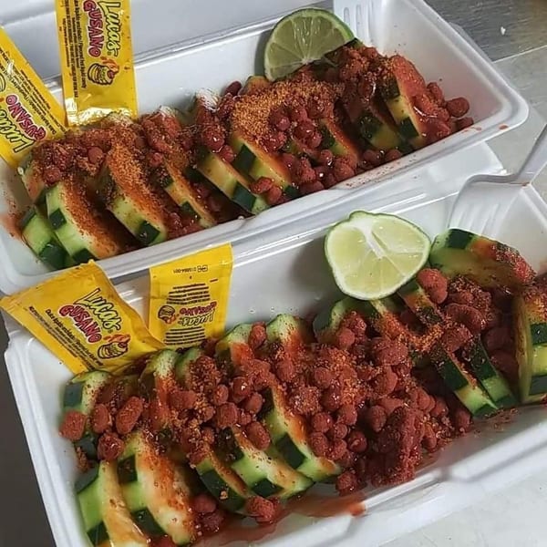 Two servings of sliced cucumbers topped with chili powder, peanuts, and lime wedges.
