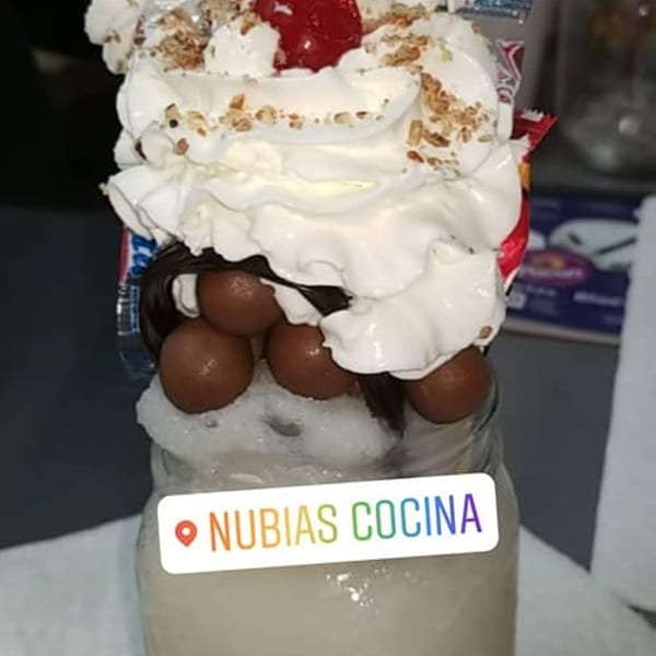 A tall dessert in a glass jar, topped with whipped cream, chocolate balls, and a cherry.