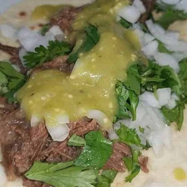 Close-up of a taco filled with shredded meat, topped with green salsa, diced onions, and cilantro.